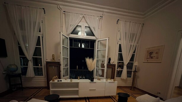 Une pièce avec un canapé blanc, une console blanche et une grande fenêtre avec des rideaux.