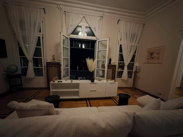 A room with a white sofa, a white console table, and a large window with curtains.