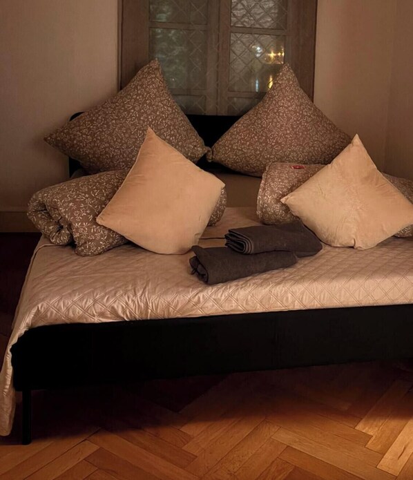 Een bed met een gewatteerde spreidek en meerdere kussens, en een opgevouwen handdoek.