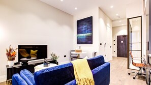 A modern living room with a blue sofa, a flat-screen TV, a coffee table, and a painting on the wall. - Hybridresi Canary Wharf (London)