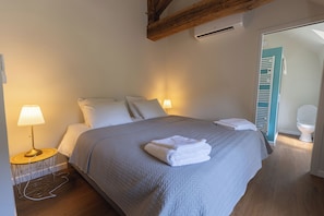 Un lit bien fait, recouvert d’une couverture grise, une lampe de chevet et un plancher en bois.