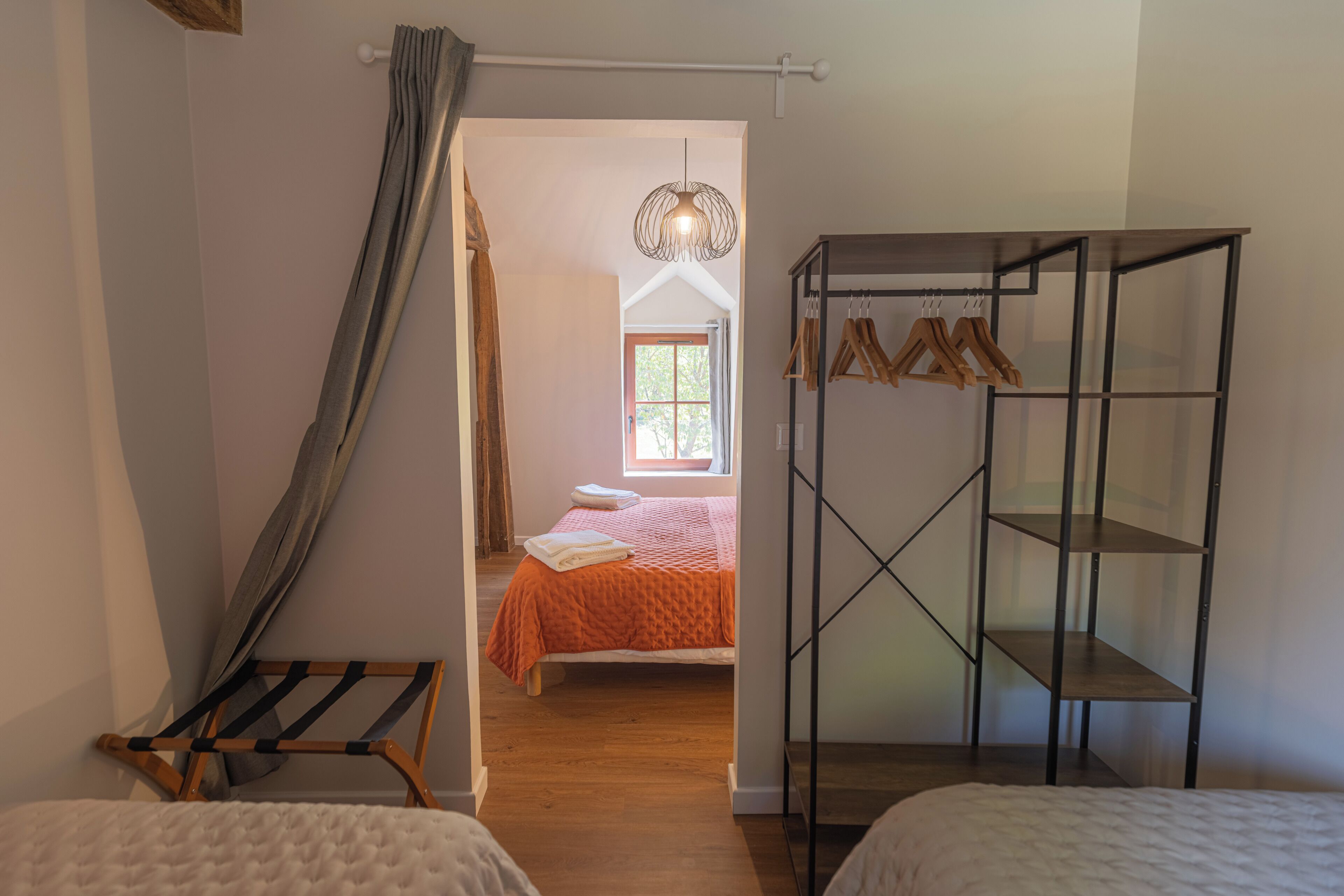 Une chambre à coucher comprenant un lit, une chaise en bois, une étagère en métal et un luminaire suspendu.