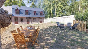 A wooden dining table with chairs, a stone wall, and a wooden fence in a backyard. - The Steward's House in Logempré—23 ha of parkland, a river, and a padel court (Pont-Saint-Pierre)