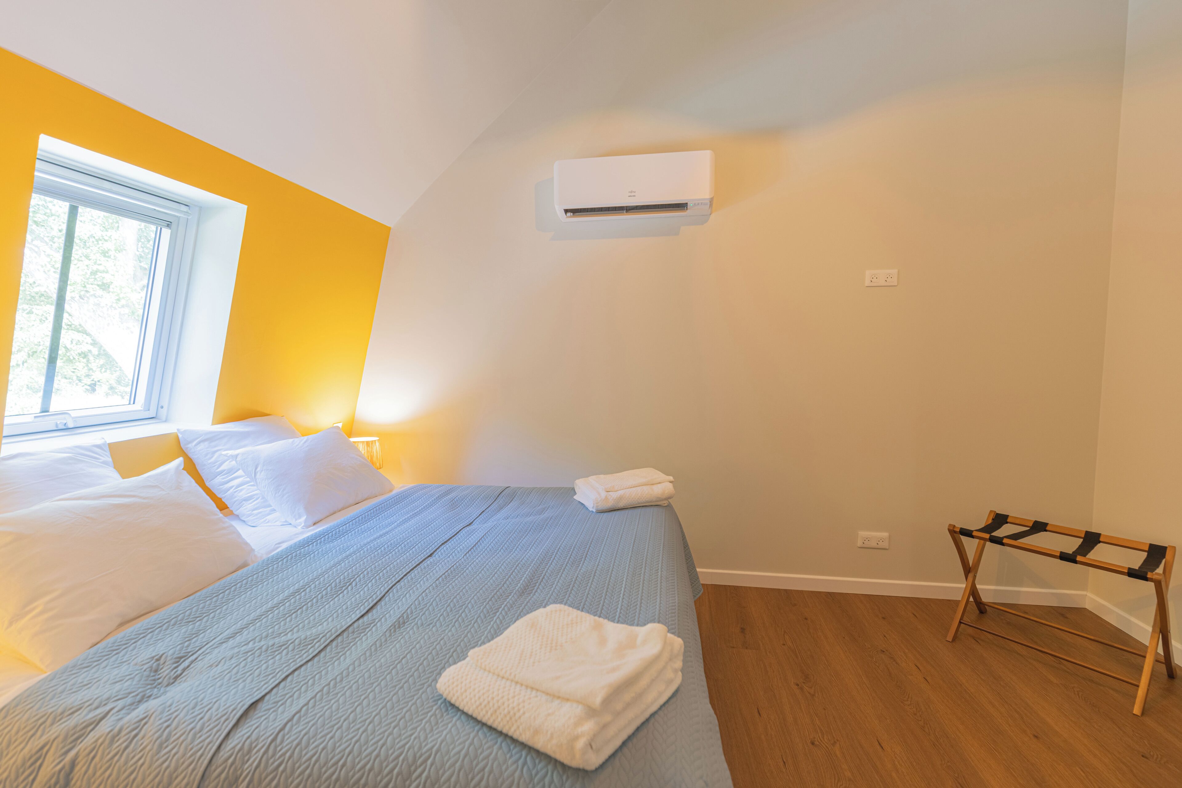 Une chambre à coucher avec un lit, une fenêtre, un appareil de climatisation et un plancher en bois.