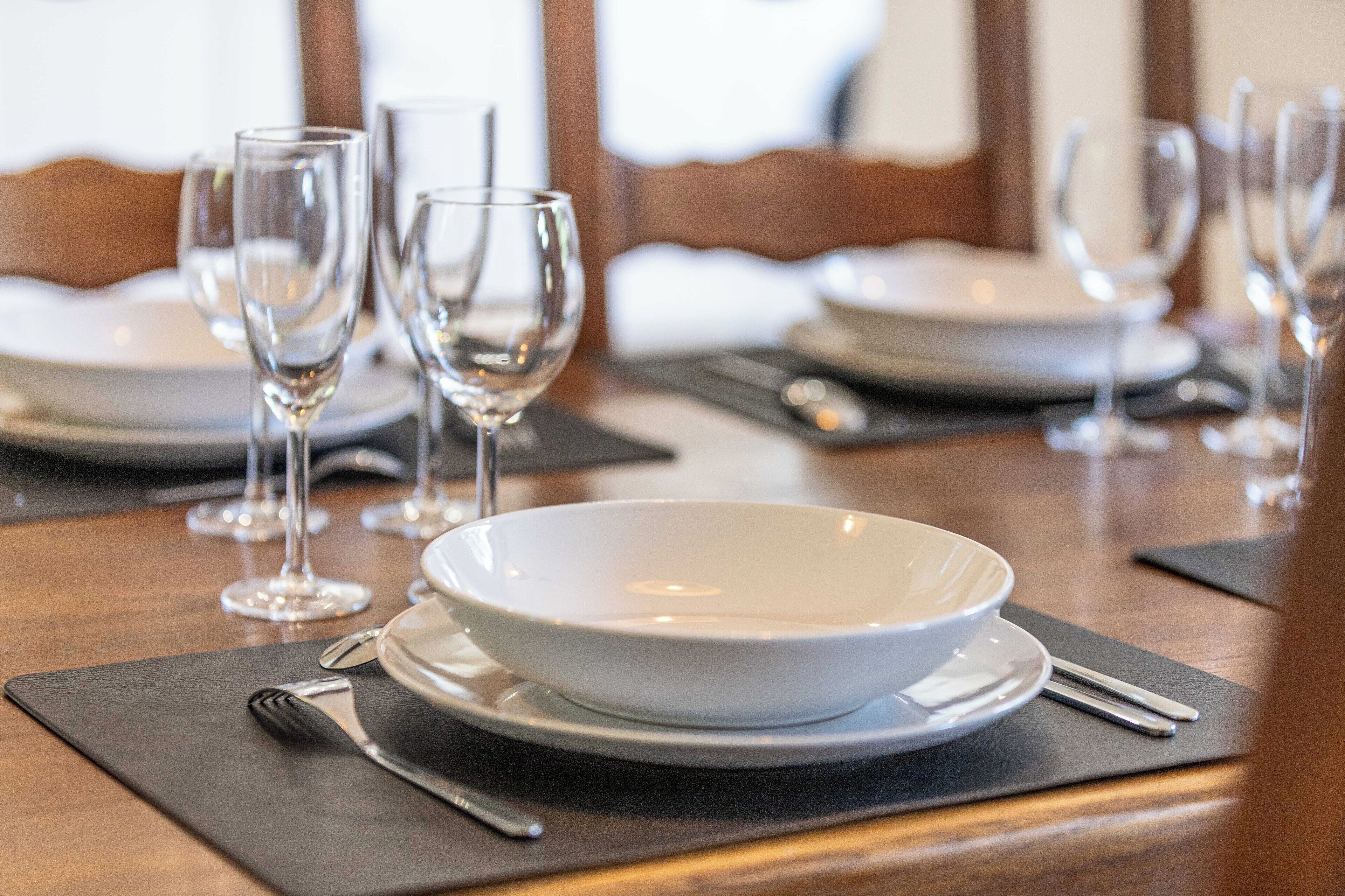 Una mesa de comedor dispuesta con platos blancos, vasos transparentes y cubiertos sobre caminos de mesa negros.