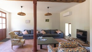 A living room with a sofa set, a coffee table, a patterned armchair, and a television. - The Steward's House in Logempré—23 ha of parkland, a river, and a padel court (Pont-Saint-Pierre)