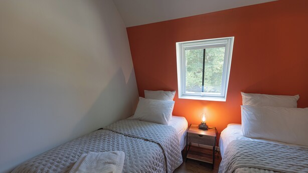 A bedroom with two single beds, a nightstand with a lamp, and a window with a view of greenery. - The Steward's House in Logempré—23 ha of parkland, a river, and a padel court (Pont-Saint-Pierre)