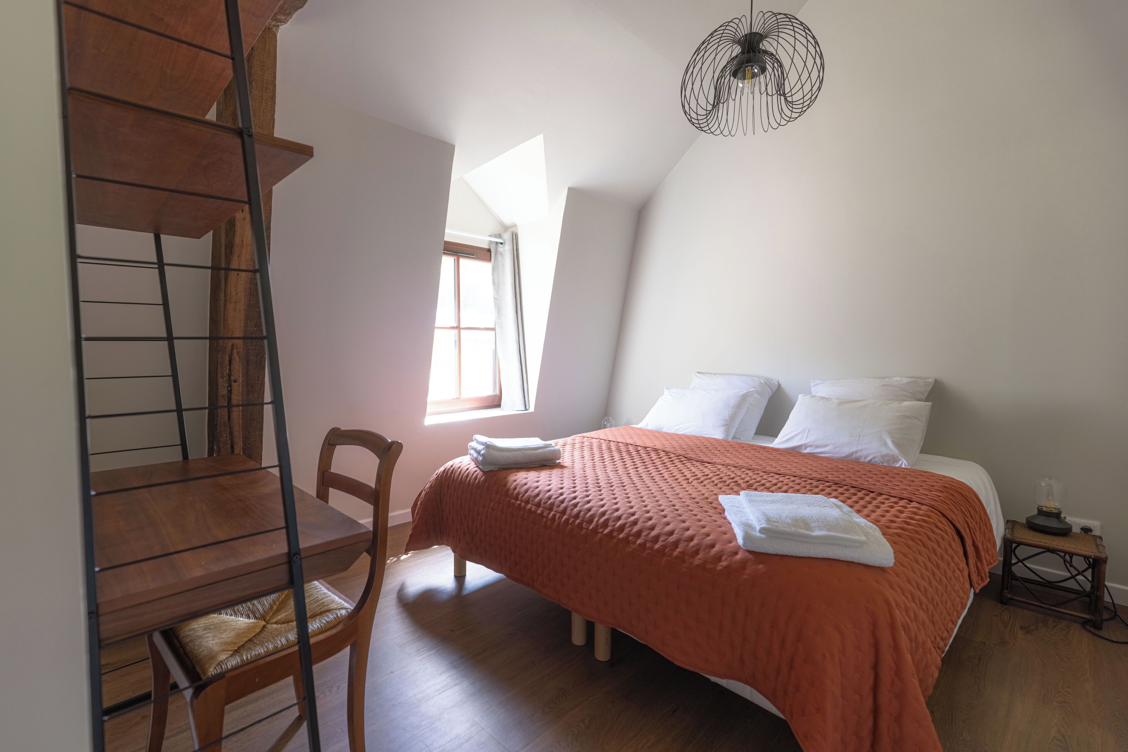A bedroom with a bed, a chair, a window, and a staircase.