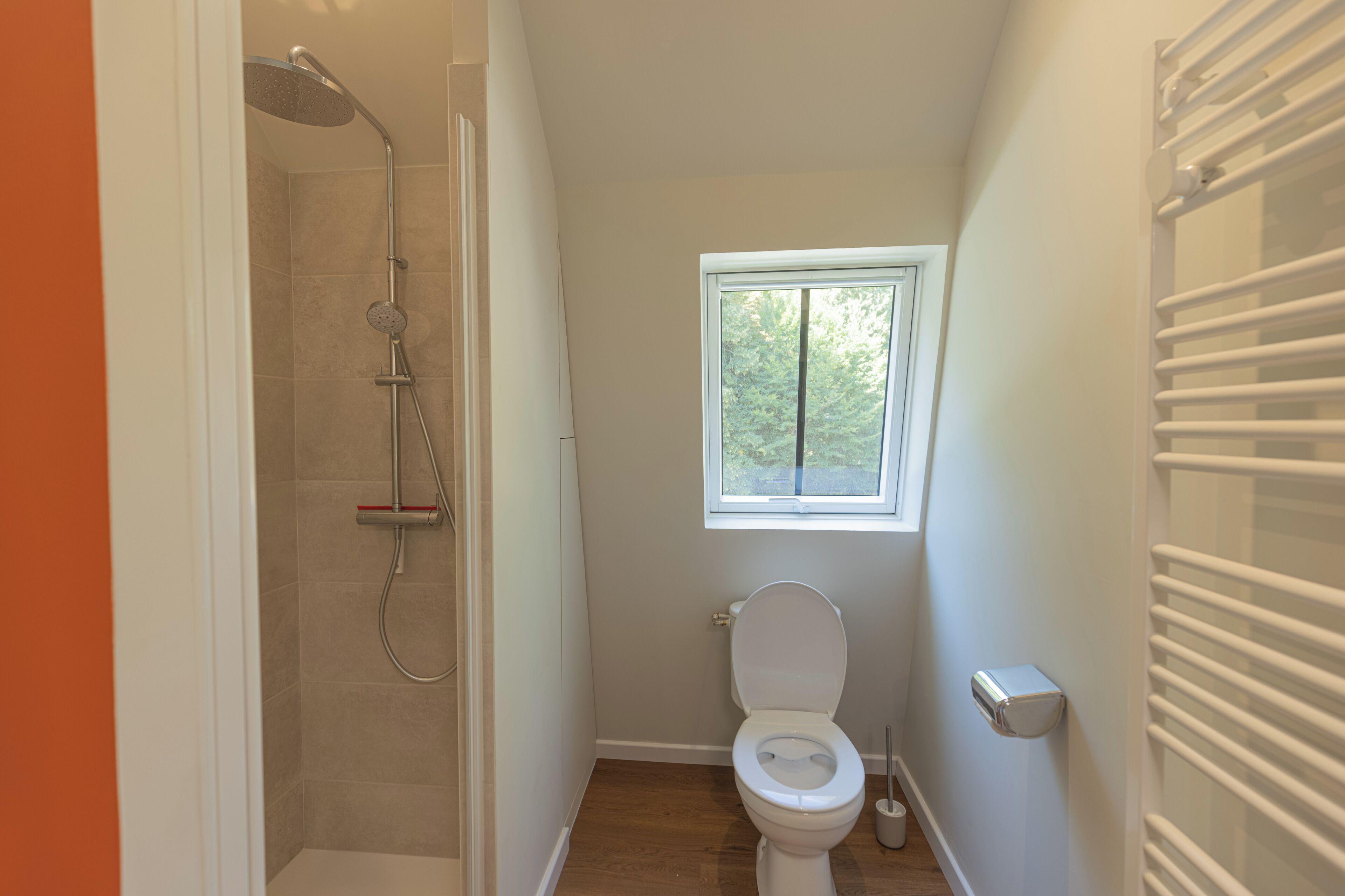 Une salle de bain compacte comprenant une douche, des toilettes et une fenêtre qui laisse entrer la lumière naturelle.