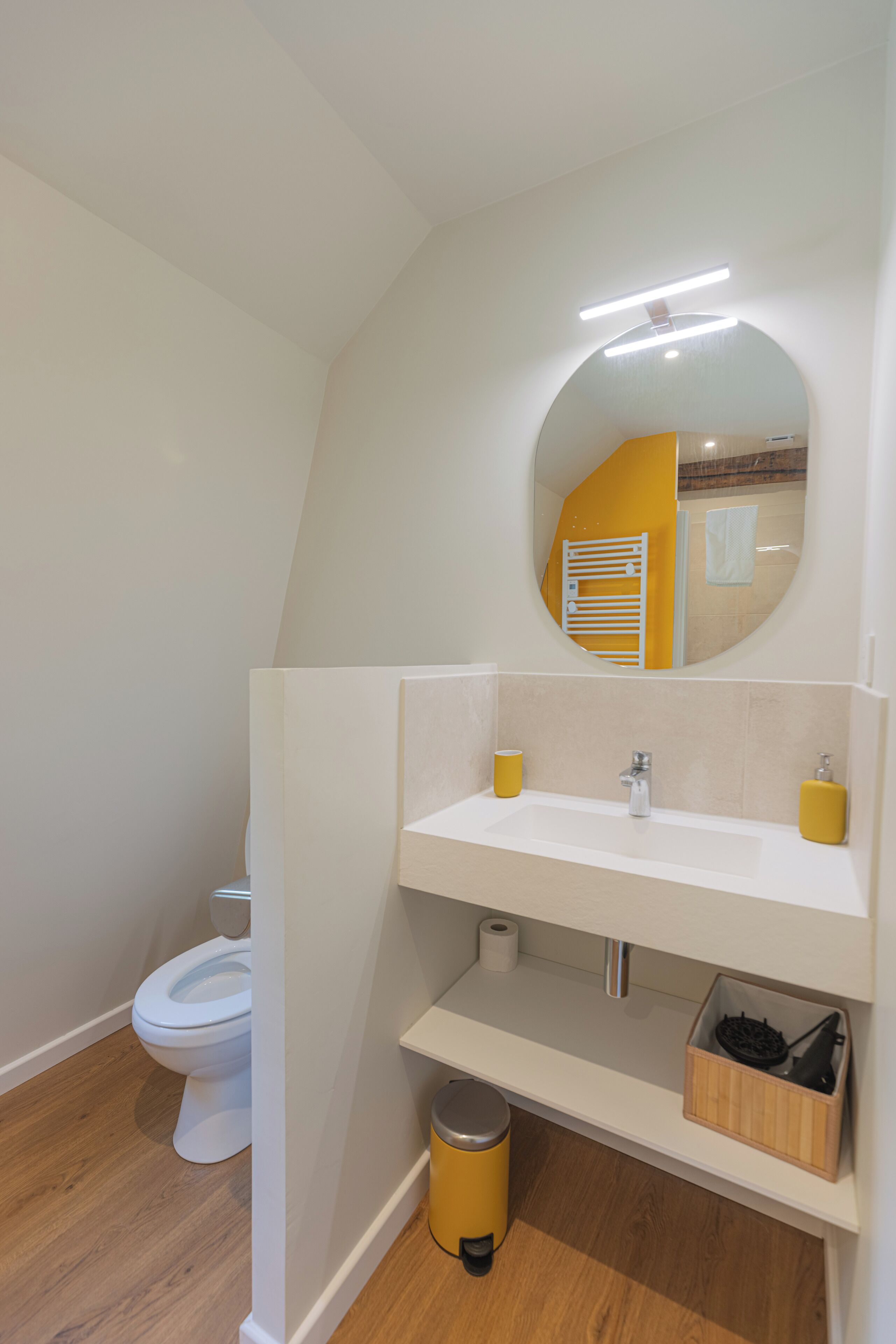 A modern bathroom with a toilet, a sink, a mirror, and a trash bin.