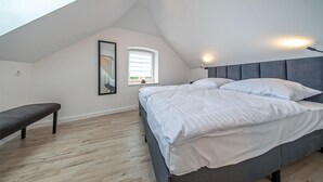 A bedroom with a bed, a bench, a window, and a wall-mounted light.