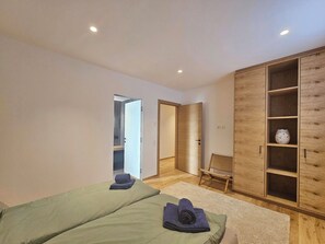 Un dormitorio con dos camas, un armario de madera, una silla y una mesita.