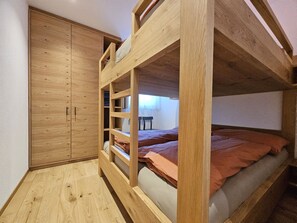 Uma cama beliche com escada de madeira, um guarda-roupa e uma pequena mesa em um quarto com piso de madeira.