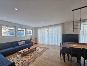 A modern living room with a sofa, coffee table, TV, dining table, and chairs. - Silberdistel EG by Interhome (Saas-Fee)