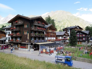 A multi-story hotel with balconies adorned with flowers, a restaurant, and a playground. - Silberdistel EG by Interhome (Saas-Fee)