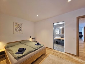 A bedroom with a bed, a chair, a painting, and a bathroom visible through an open door. - Silberdistel EG by Interhome (Saas-Fee)