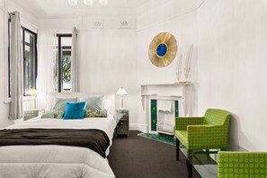 A hotel room with a bed, a nightstand, a lamp, a green armchair, a fireplace, and a decorative wall piece. - Spacious 4-bed Character House in Vibrant Stanmore (Sydney)