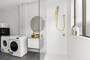 A modern bathroom with a washing machine, a gold sink, and a shower with a golden showerhead. - Spacious 4-bed Character House in Vibrant Stanmore (Sydney)