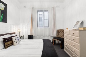 Een hotelkamer met een bed, een stoel, een dressoir en een raam met gordijnen.