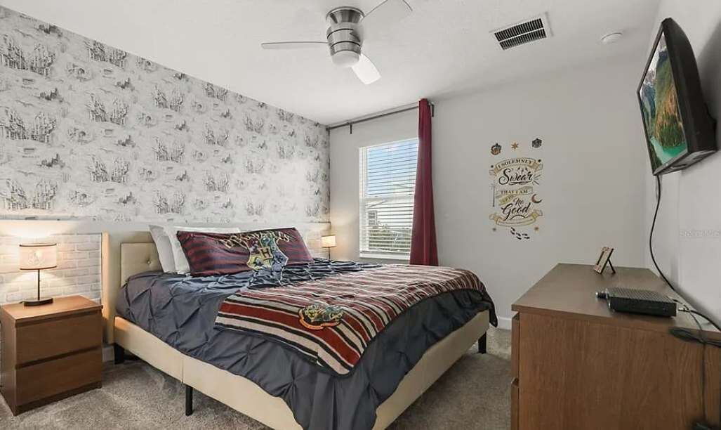 A bedroom with a bed, nightstands, a desk, a ceiling fan, and a window with blinds.