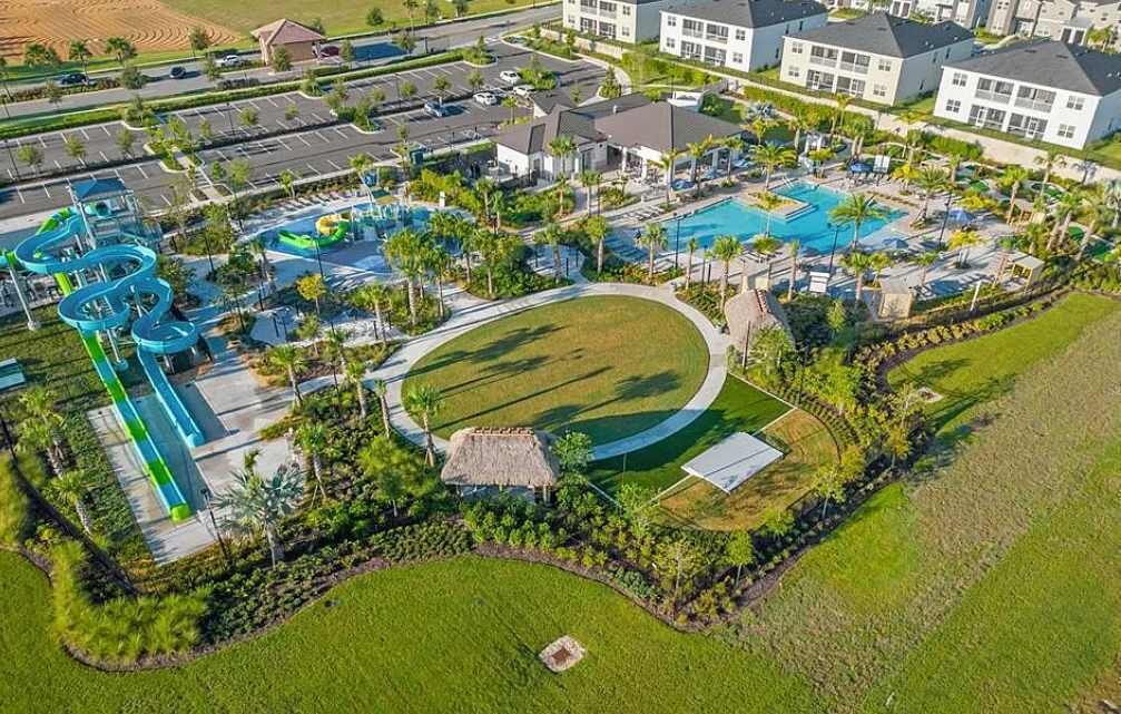 An aerial view of a resort with a swimming pool, water slides, and a well-maintained lawn.