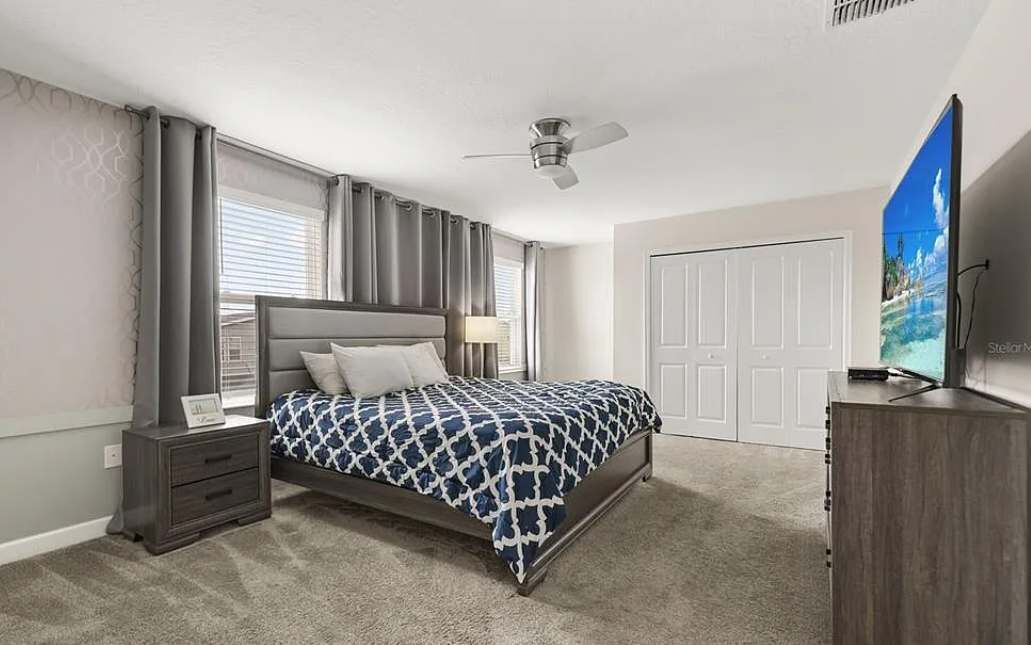 A bedroom with a bed, nightstand, dresser, ceiling fan, and a painting on the wall.