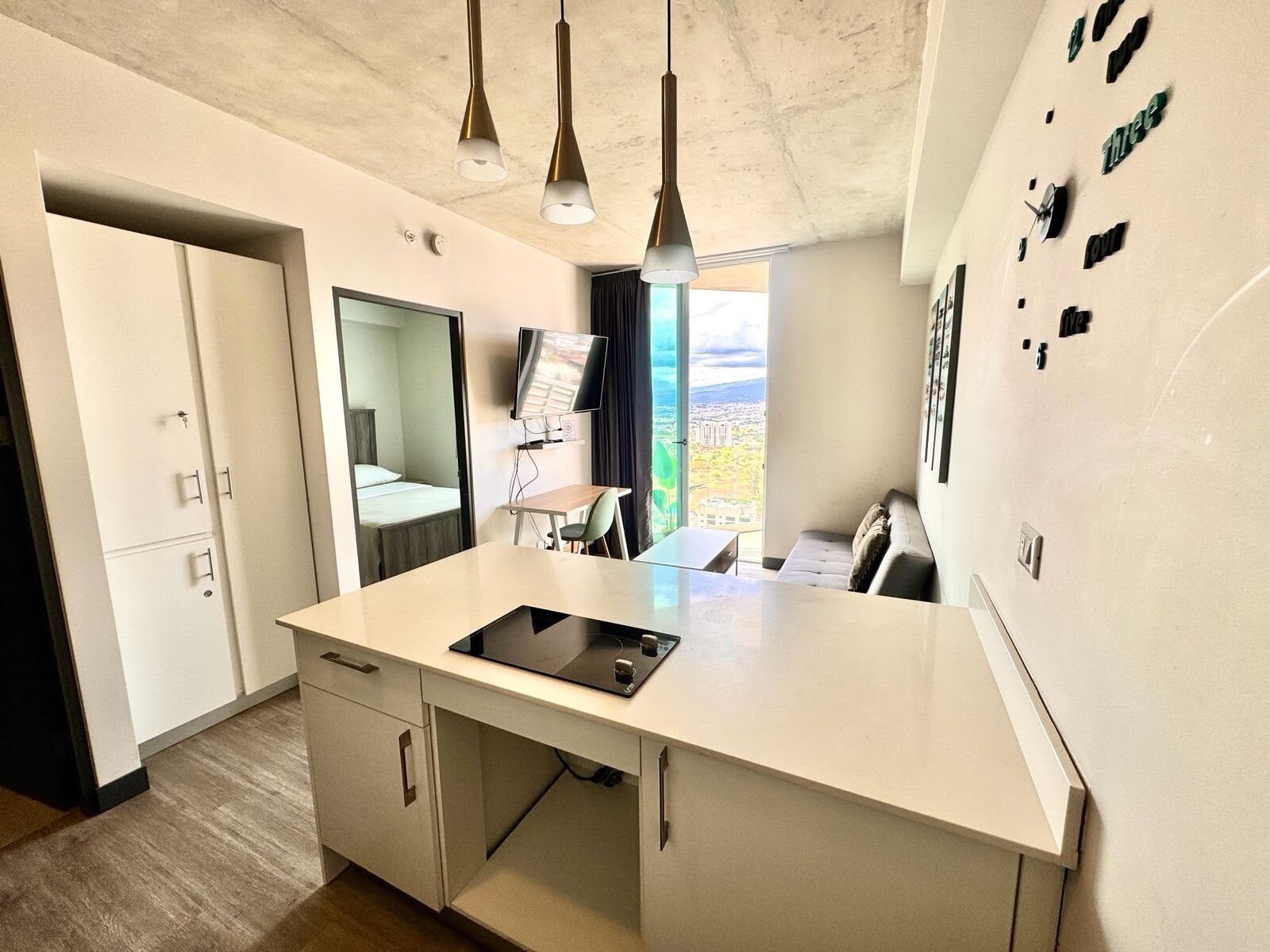 Ein modernes Hotelzimmer mit einer großen Kücheninsel, einem Flachbildfernseher, einem Essbereich und Blick auf die Stadt.