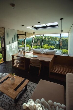 A modern room with a large window, a wooden desk, a sofa, and a coffee table.