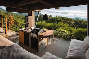 Un área de cocina al aire libre con parrilla, pileta y espacio para comer, con vistas a un paisaje verde y exuberante.