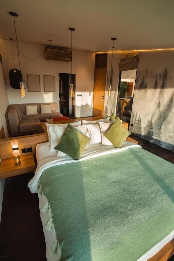 A modern bedroom with a bed, bedside tables, a sofa, and a painting of trees.