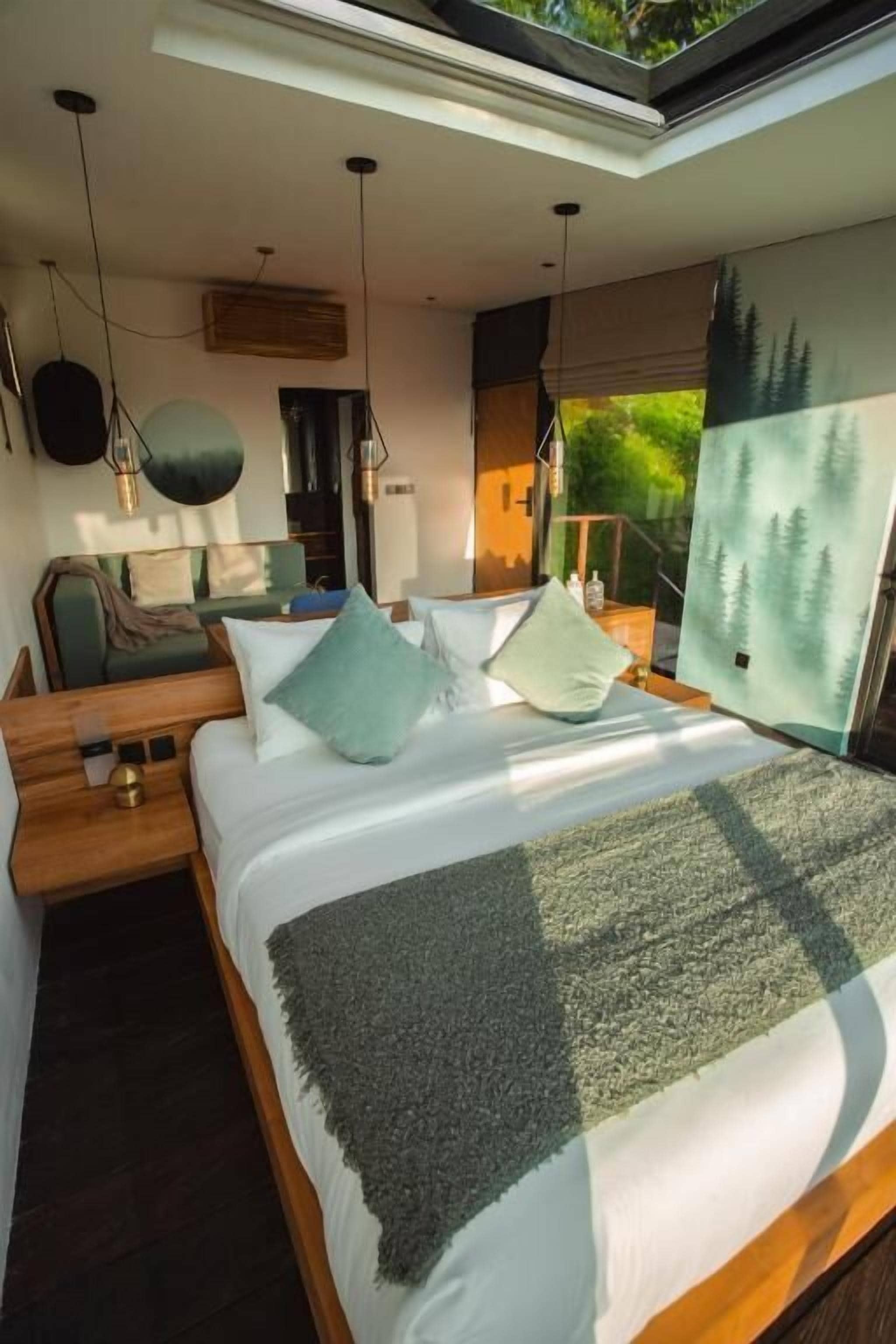 A modern bedroom with a skylight, a bed with a checkered throw, and a forest-themed wall mural.