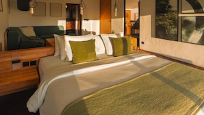 Quarto de hotel moderno com uma cama grande, um sofá verde e uma mesinha de cabeceira de madeira.