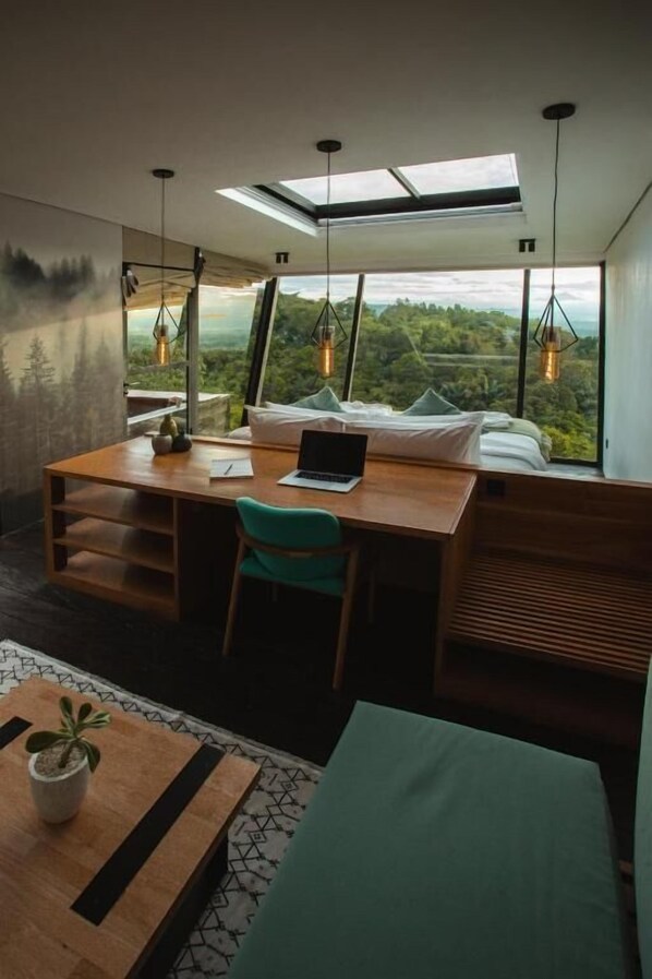 A modern bedroom with a skylight, a desk with a laptop, and a view of the outdoors.