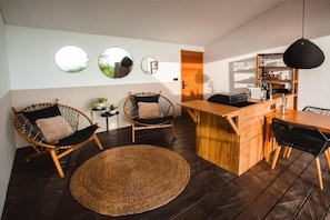 A modern interior with a wooden dining table, two wicker chairs, a woven rug, and a bar area.