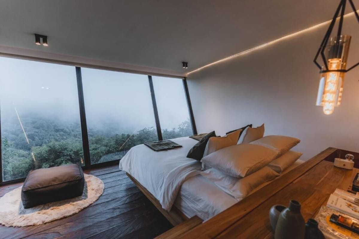 Un dormitorio moderno con una cama grande, suelo de madera y vistas al bosque a través de amplios ventanales.