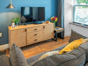 A modern living room with a wooden herringbone cabinet, a flat-screen TV, a small side table, and a sofa with cushions. - 1 bedroom accommodation in Kingskettle (Kingskettle)