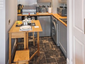 A compact kitchen with a wooden table set for dining, a washing machine, and a microwave. - 1 bedroom accommodation in Kingskettle (Kingskettle)