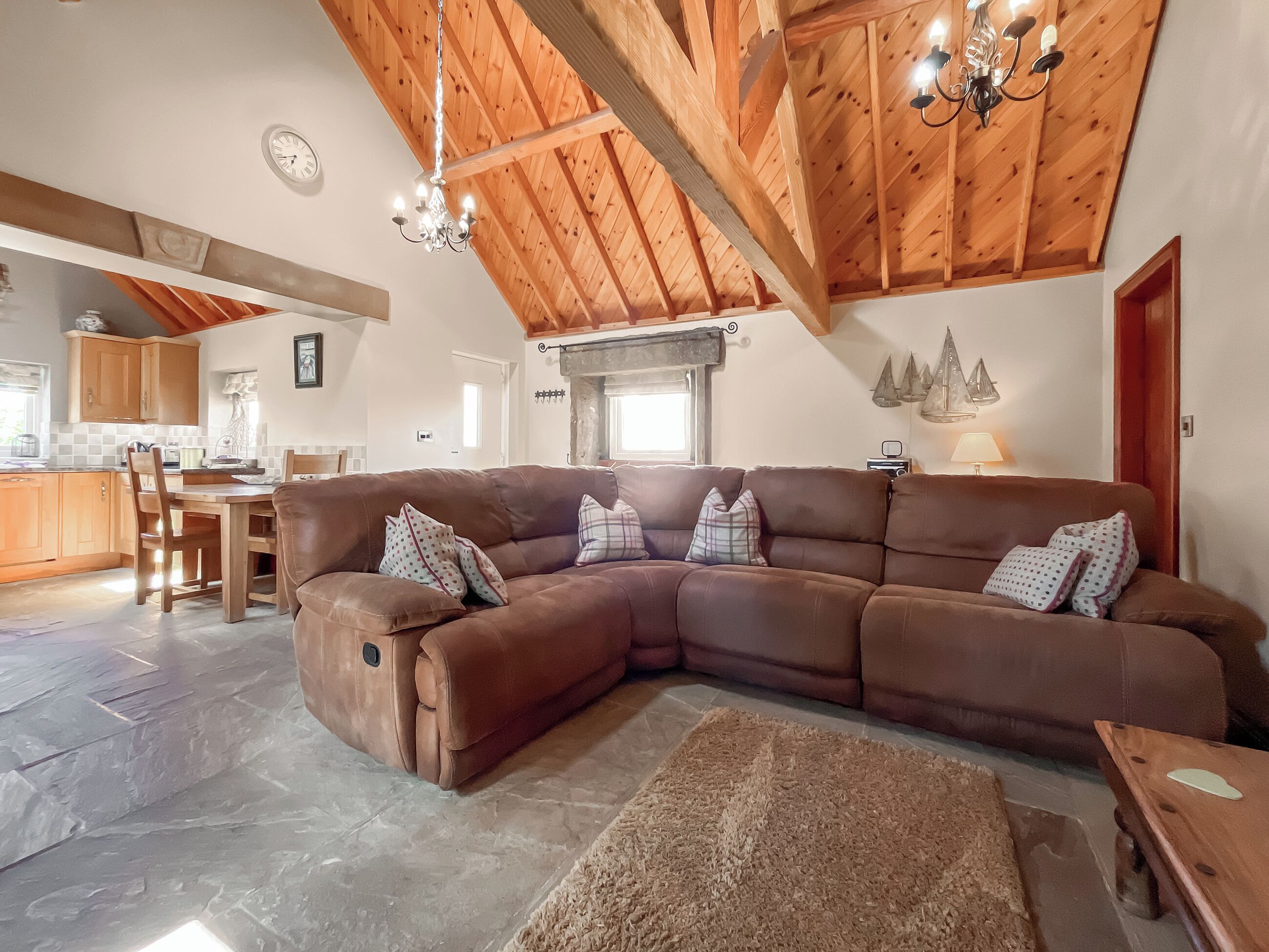 A spacious living area with a large brown sectional sofa, a wooden ceiling, and a kitchen in the background.