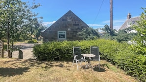 Un edificio in pietra con un tetto triangolare, un quadro incorniciato e un piccolo tavolo con sedie davanti.