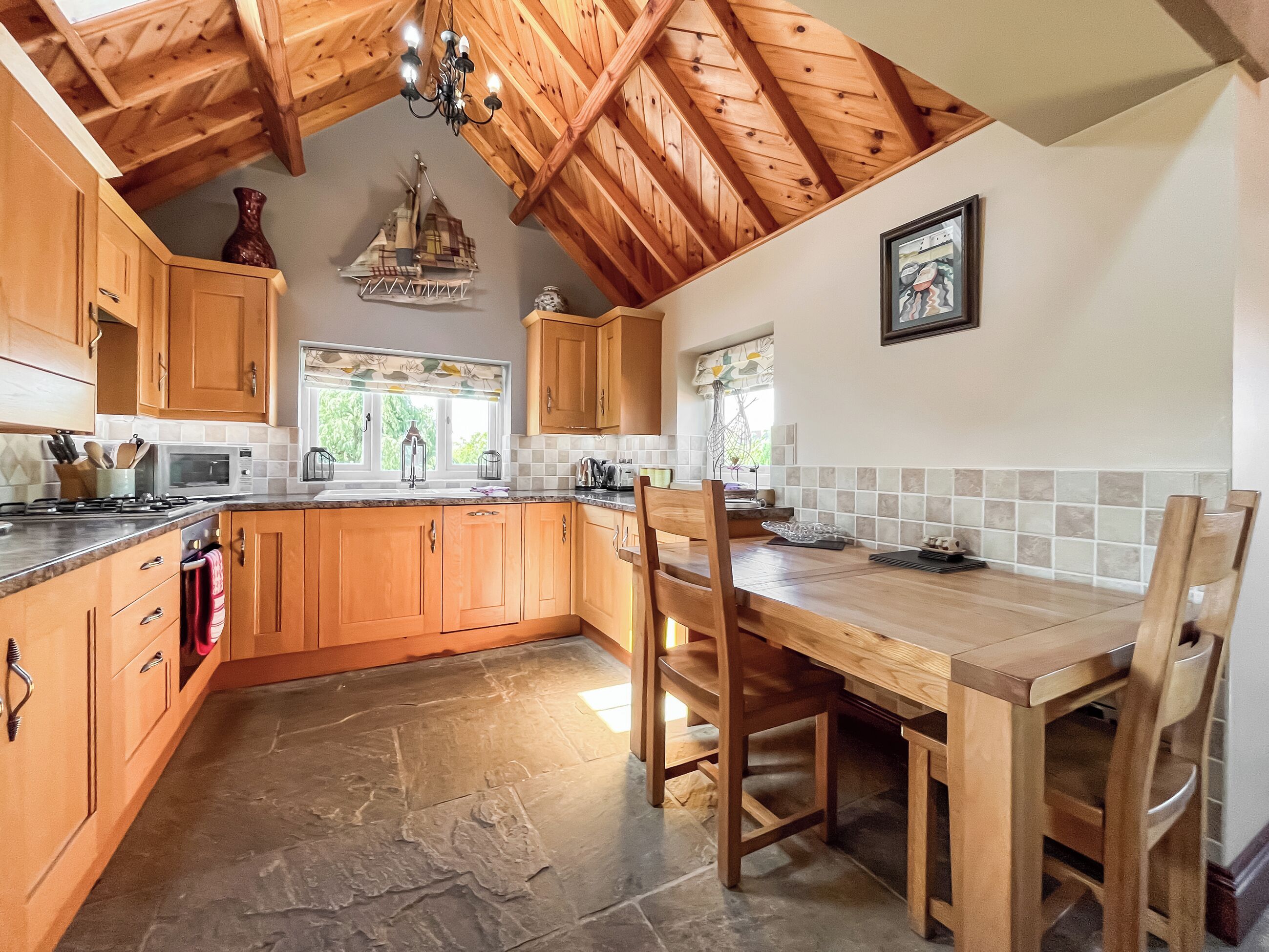 A kitchen with wooden cabinets, a stone floor, and a dining area with a table and chairs.