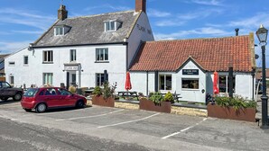 Un edificio a due piani con un cartello che riporta 'FLASK INN' e un'auto rossa parcheggiata di fronte.