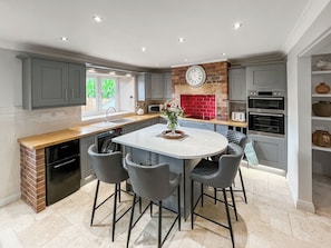 A modern kitchen with grey cabinetry, a central island with bar stools, a red brick backsplash, and built-in appliances. - 2 bedroom accommodation in Hamsterley, near Bishop Auckland (Hamsterley, near Bishop Auckland)