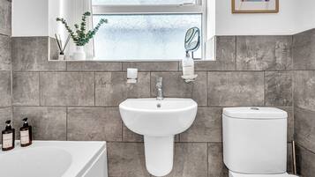 A bathroom with a white sink, a toilet, and a bathtub. There is a window with frosted glass, a mirror, and a framed picture on the wall.