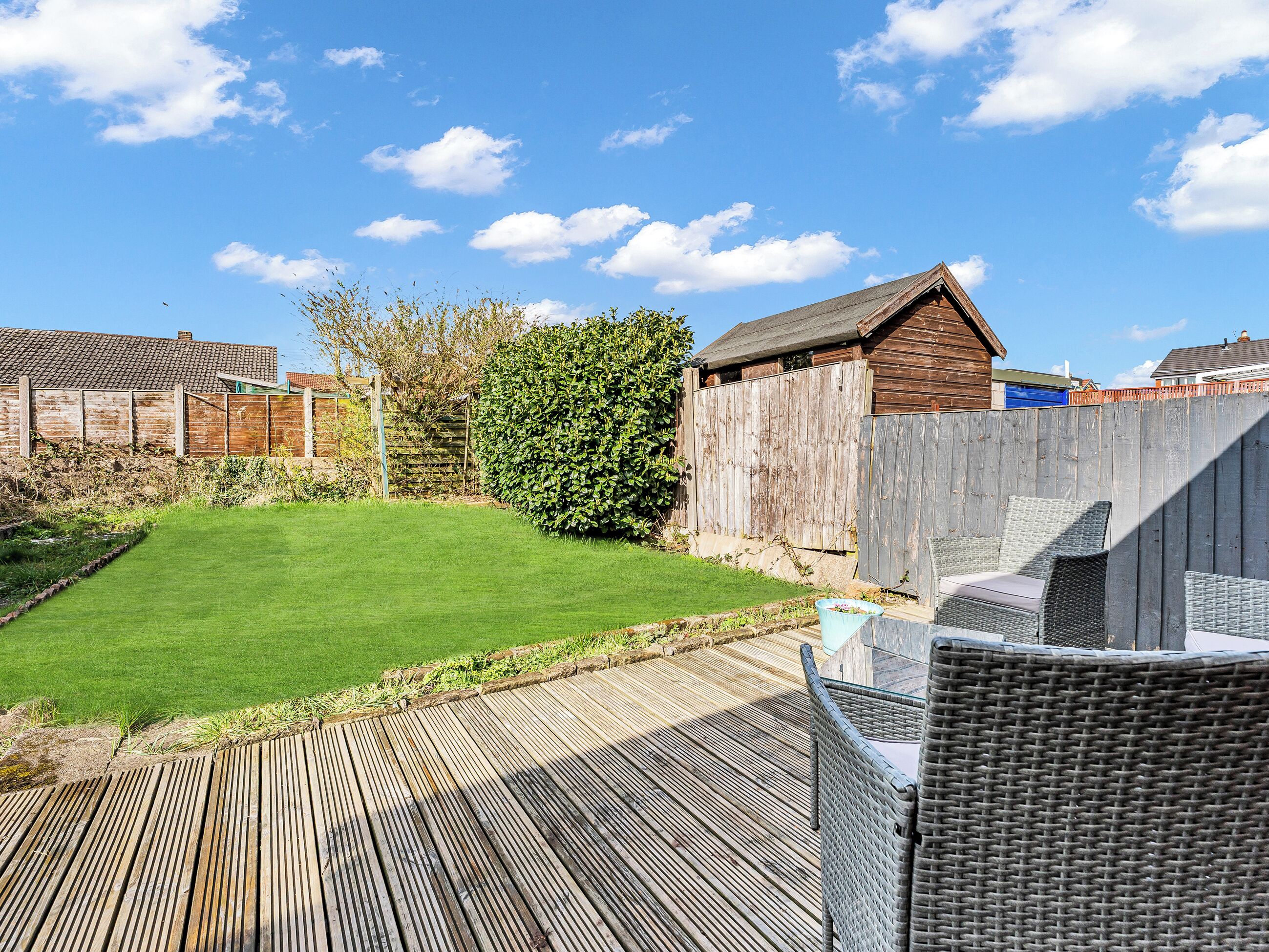 A backyard with a wooden deck, a grassy lawn, a wooden fence, and a shed.