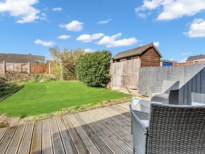 A backyard with a wooden deck, a grassy lawn, a wooden fence, and a shed.