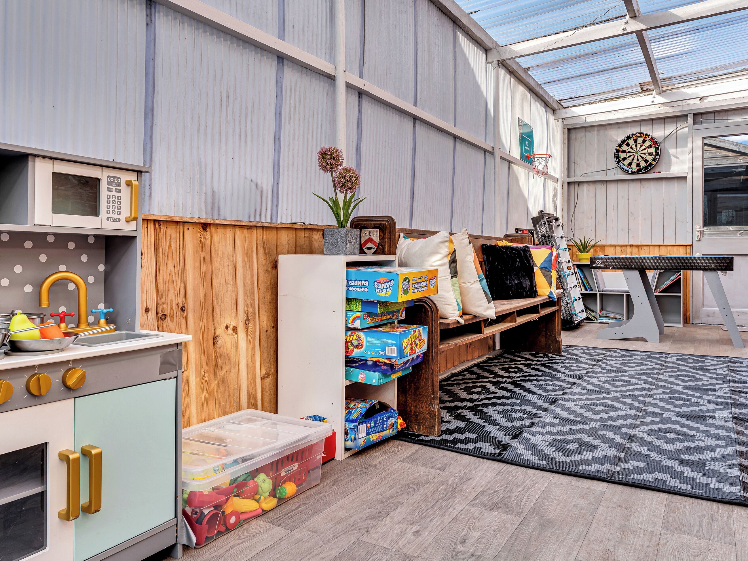 A playroom with a kitchen area, a dartboard, and a ping pong table.
