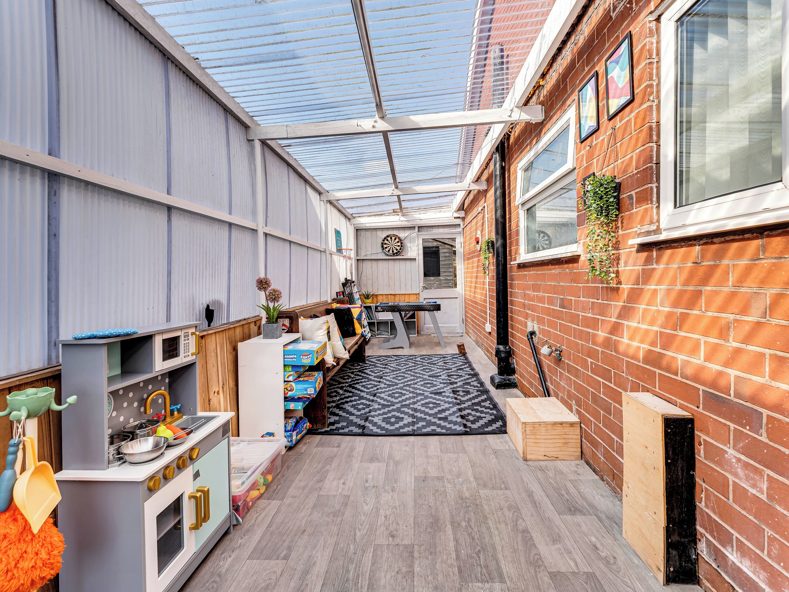 A narrow indoor space with a kitchen area, a dartboard, and a patterned rug.