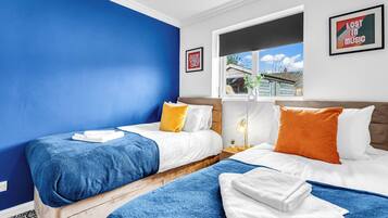 Quarto de hotel com duas camas, uma janela com vista, um quadro na parede e uma mesa de cabeceira com abajur.