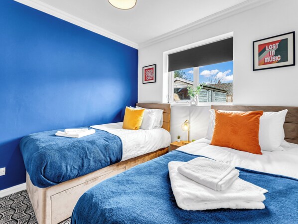 A hotel room with two beds, a window with a view, a wall with a framed picture, and a bedside table with a lamp.