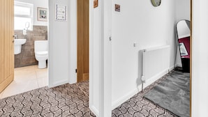 Un couloir avec un tapis à motifs, un radiateur et une horloge au mur.